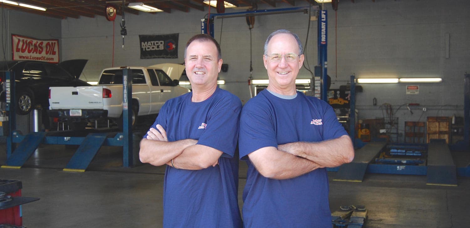 Gene and John Kobar standing in front of vehicles on lifts